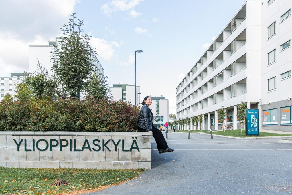 Henkilö istuu Ylioppilaskylä-kyltillä